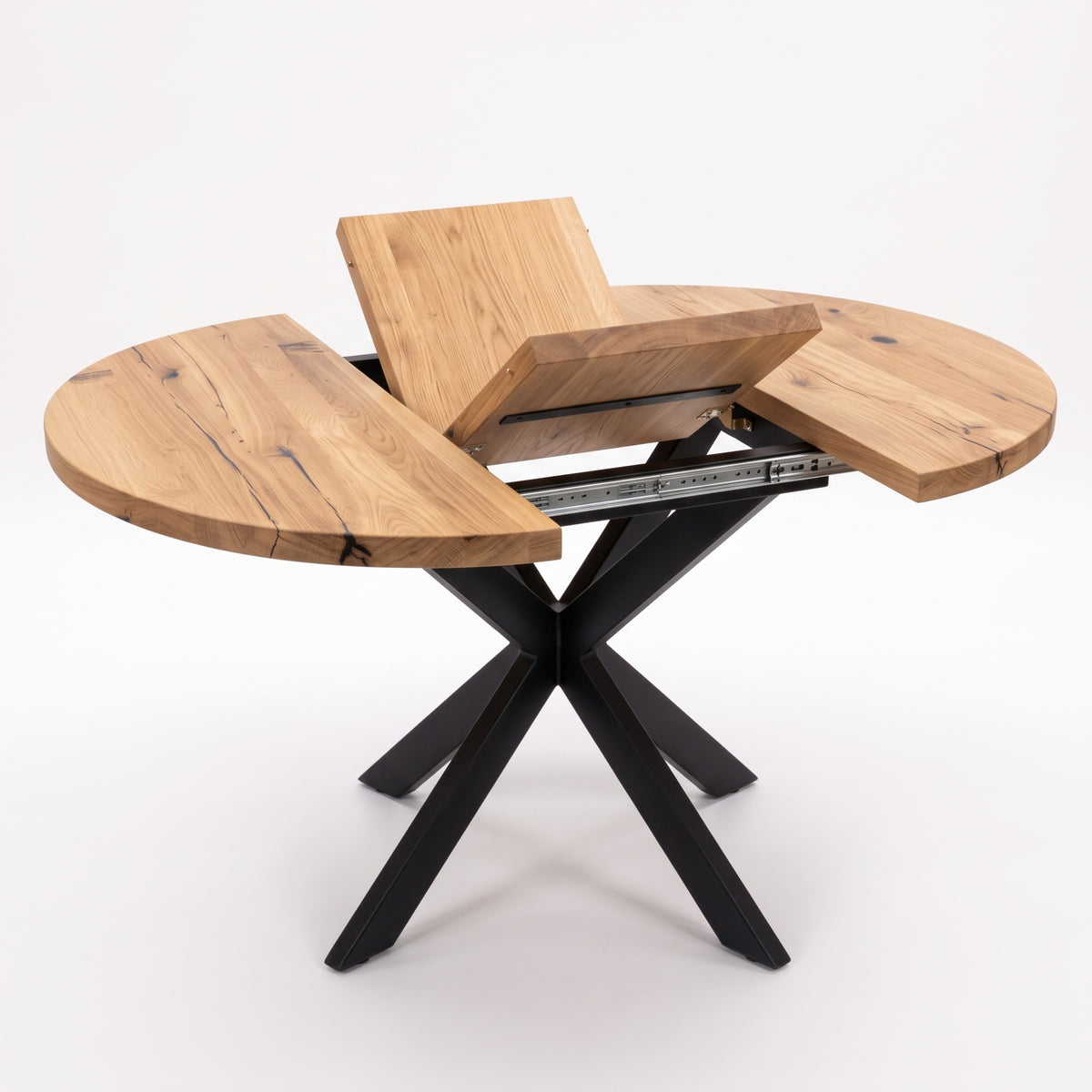 A modern round dining table with a natural wood grain top and a black metal X-shaped base, shown with the center panel raised to reveal the table's extension mechanism.
