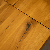 Close-up of a warm honey-toned wooden tabletop with visible wood grain, knots, and a dark seam between joined panels.
