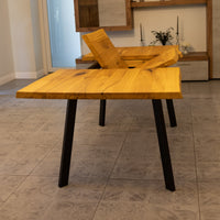 A rustic wooden dining table with a live-edge top and black metal legs, shown in a modern dining room setting.