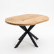 An oval wooden dining table with a natural oak finish and a black metal X-shaped base, shown on a clean white background.