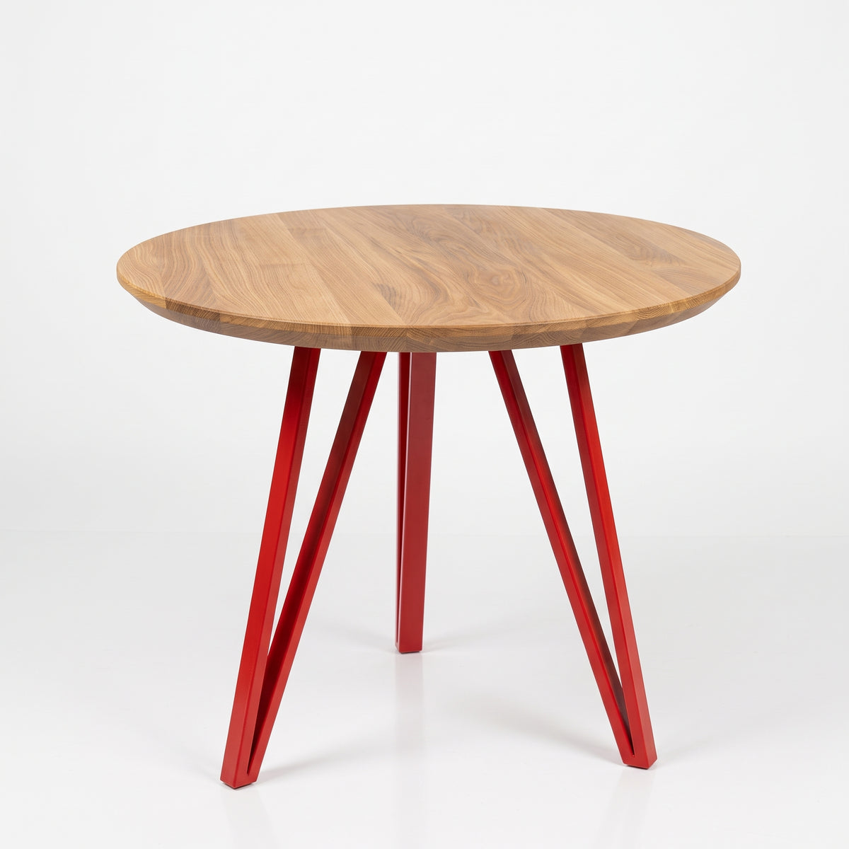A round wooden dining table with a warm medium-brown wood grain top and three glossy red metal legs, shown on a clean white studio background.