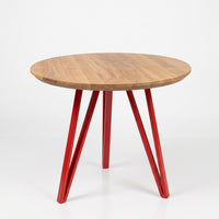 A round wooden dining table with a warm medium-brown wood grain top and three glossy red metal legs, shown on a clean white studio background.