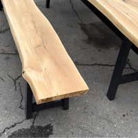 A live-edge natural wood bench with a black metal frame, shown next to a matching wooden table on a gray concrete surface.