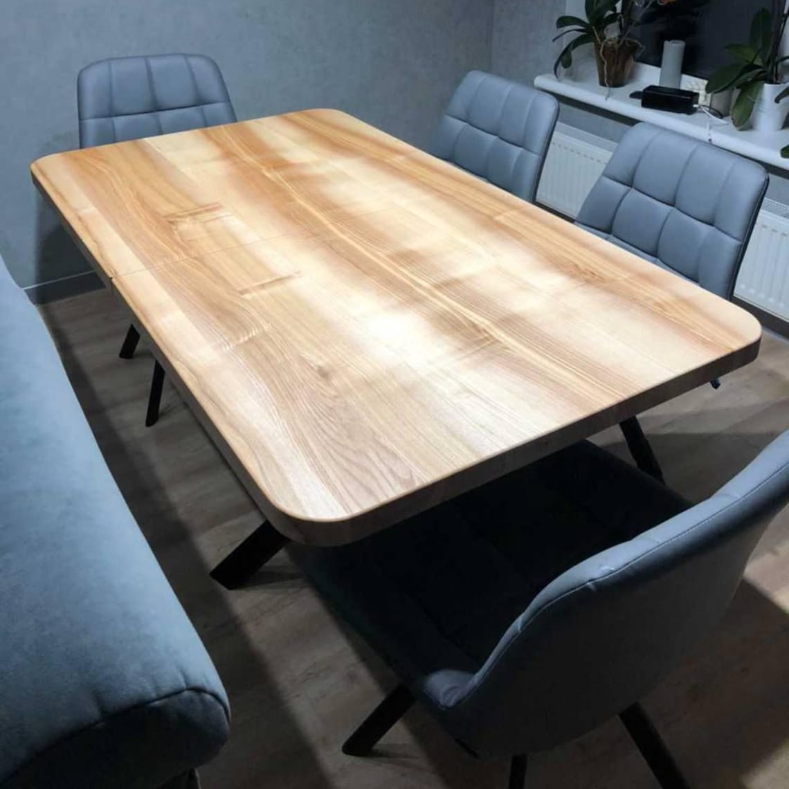 A rectangular wooden conference table with a light natural wood finish, surrounded by gray upholstered chairs in a modern office or meeting room setting.