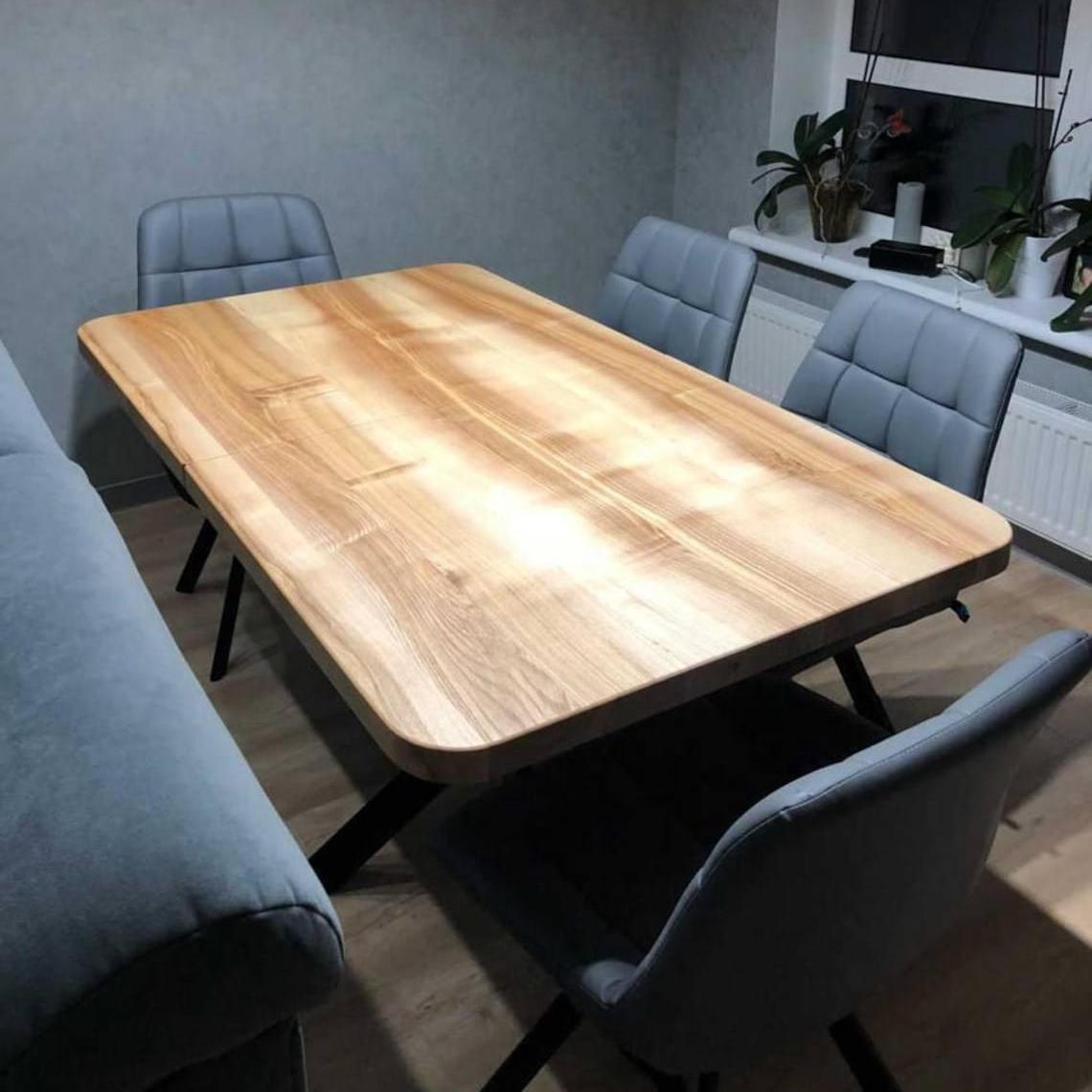 A rectangular wooden dining table with rounded corners and black metal legs, surrounded by gray upholstered chairs in a modern dining room setting.