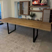 A large rectangular wooden dining table with a live-edge rustic top and black metal U-shaped legs, shown in a modern living room setting with patterned gray floor tiles.