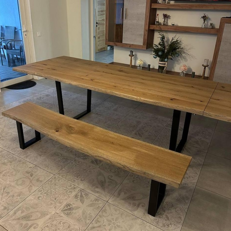 A rustic wooden dining table with a live-edge slab top and matching bench, supported by black metal legs, shown in a home interior setting.