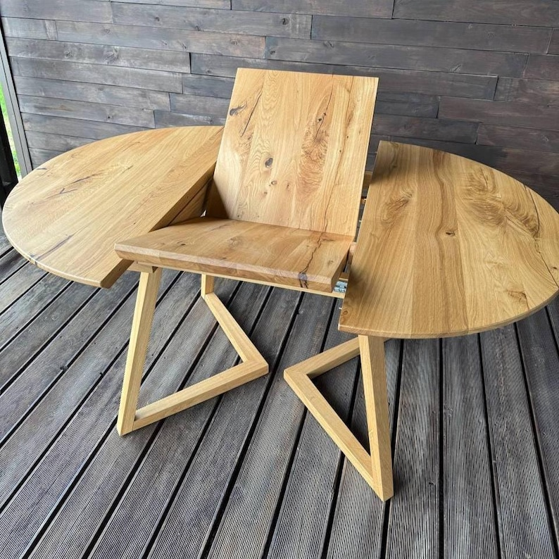 A light natural wood folding table with a matching folding chair, set on a gray wooden deck with a dark wood paneled wall background.