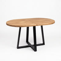 An oval wooden dining table with a light brown wood grain top and a black metal geometric base, shown on a clean white background.