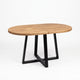 An oval wooden dining table with a light brown wood grain top and a black metal geometric base, shown on a clean white background.